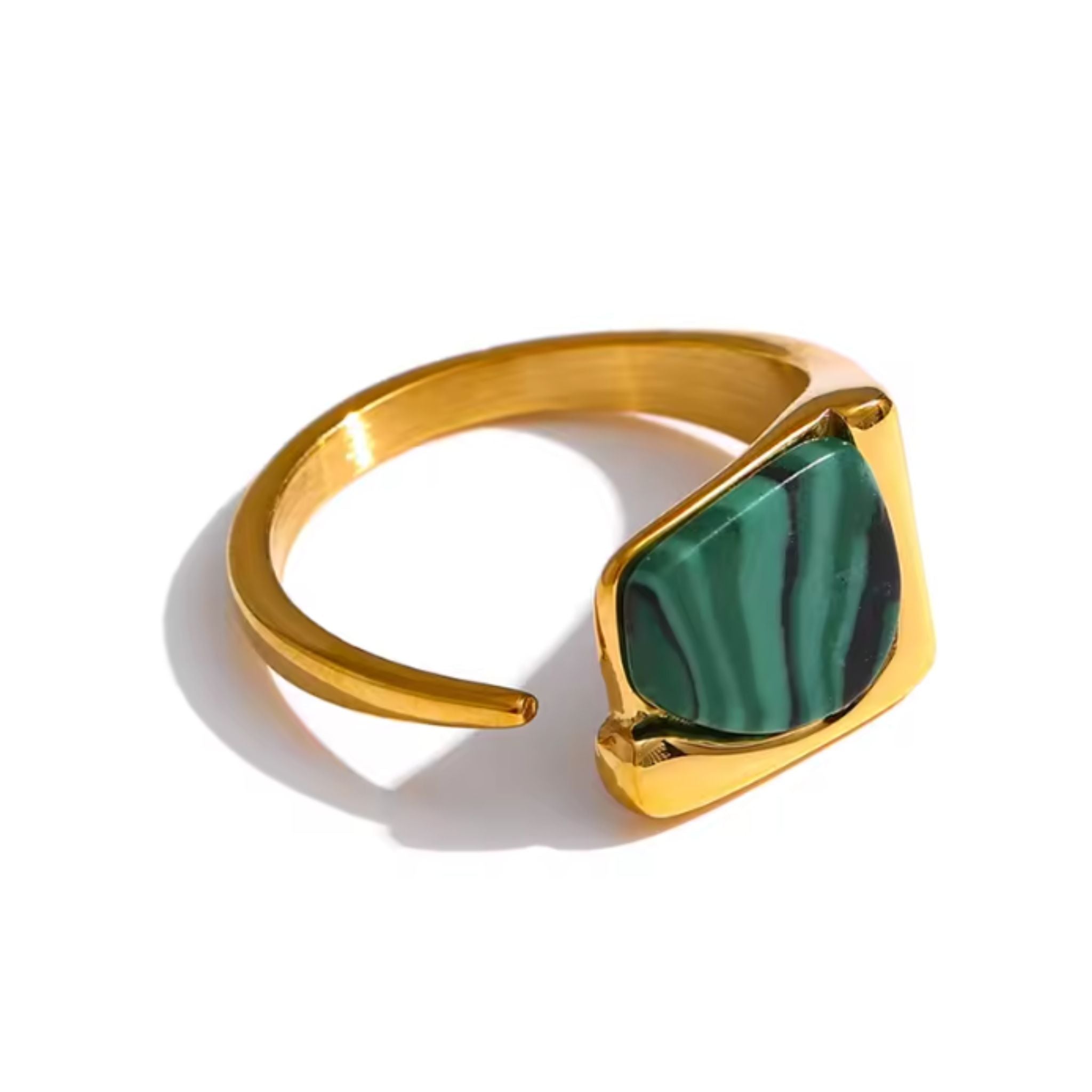 Vue de trois-quarts d'une bague chevalière en métal doré brillant avec un anneau fin et ouvert. Le plateau asymétrique est orné d'une pierre plate de Malachite d'un vert intense avec des bandes noires parallèles. Le bijou est photographié sur un fond blanc neutre, mettant en avant la finesse de l'anneau et le poli du métal.