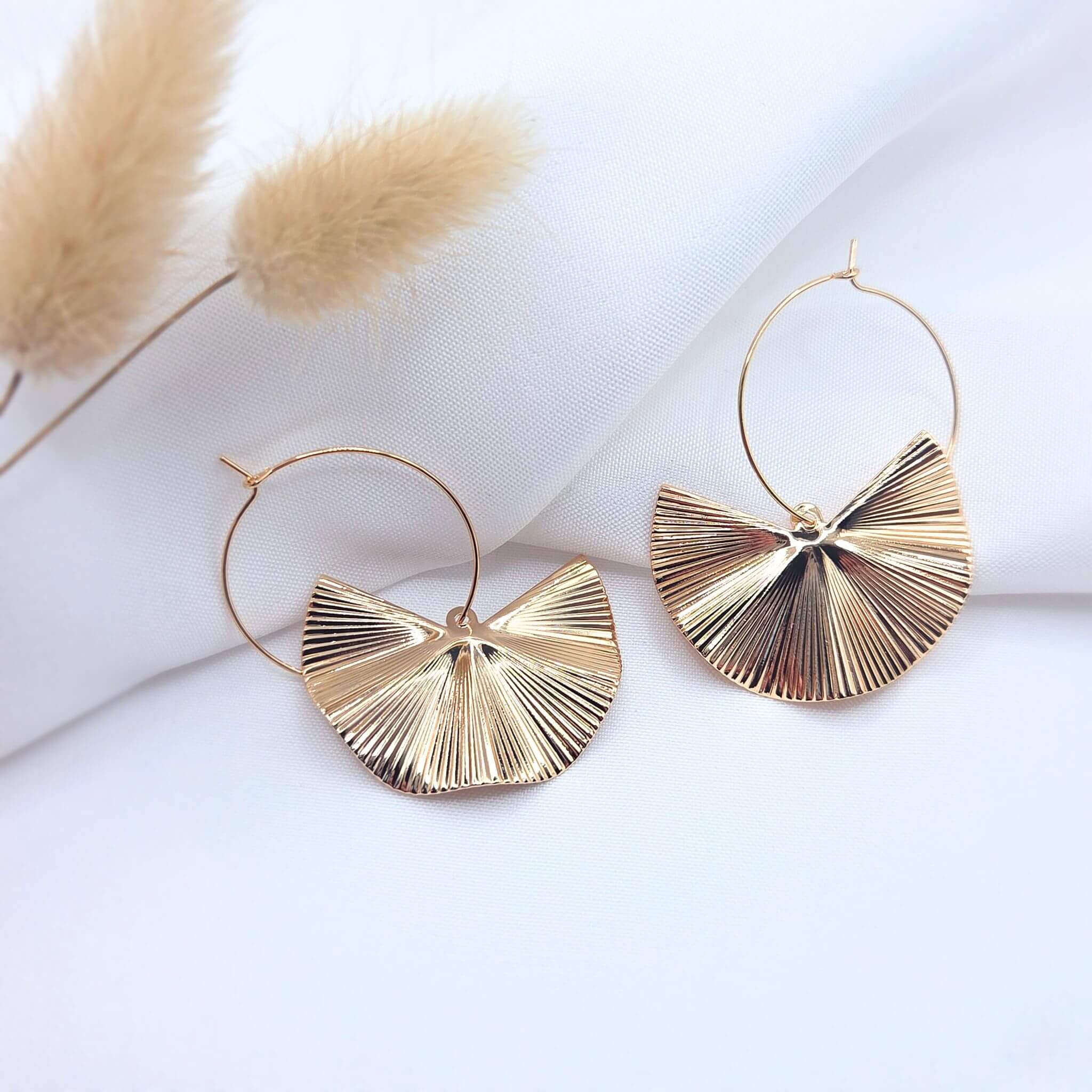 Créoles dorées avec pendentifs demi-lune texturés de style éventail sur fond blanc élégant.