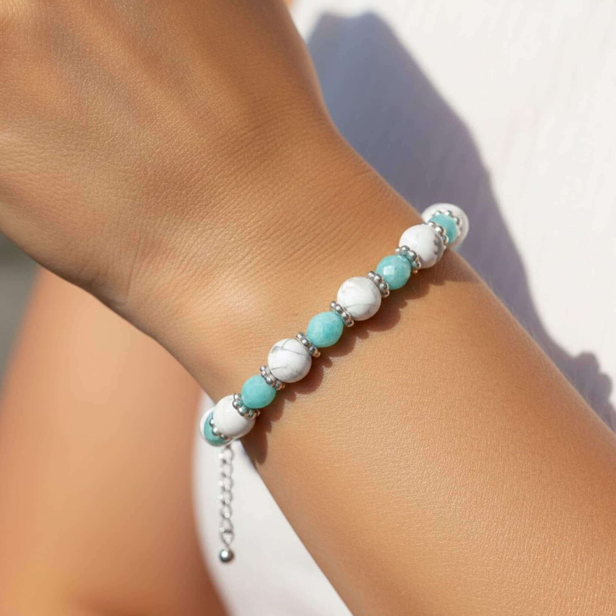 Photo portée du bracelet GIA de MilyGlowUp au poignet d'une femme. On y voit l'alternance des perles de Howlite blanche et d'Amazonite turquoise facettée, séparées par des anneaux argentés. Le bracelet est ajusté grâce à sa chaînette d'extension en acier inoxydable.