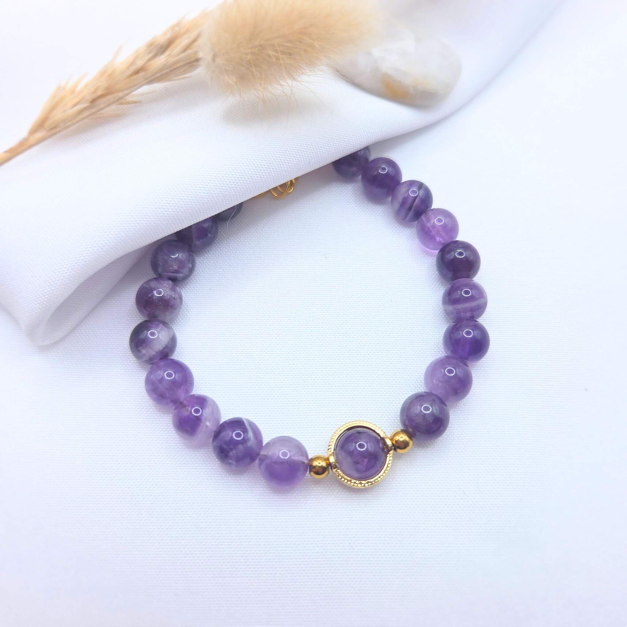 Bracelet en perles d'améthyste naturelle violette avec un médaillon central doré et un fermoir mousqueton en or, présenté sur un fond blanc.