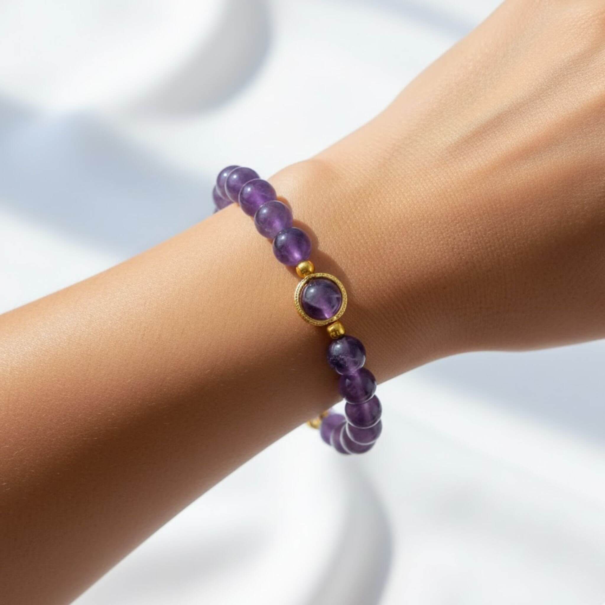 Vue rapprochée du bracelet Nora en améthyste porté au poignet, révélant l'éclat des perles violettes et du médaillon doré sous une lumière naturelle.