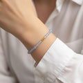 Vue rapprochée du poignet d'une personne portant un bracelet fin en aigue marine bleue. Les perles rondes et translucides d'un bleu pastel entourent le poignet, avec trois petites perles dorées centrales qui captent la lumière. La personne porte une chemise blanche boutonnée, créant un look doux, lumineux et épuré.