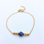 Bracelet fin en chaîne dorée avec une pierre centrale en Lapis-lazuli bleu brut et perles dorées géométriques.