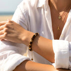 Look bohème d'été : bracelet de perles marron œil de tigre porté à la plage avec des bijoux dorés et une tenue décontractée.