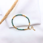 Bracelet fin en perles de malachite verte et billes dorées avec fermoir ajustable.