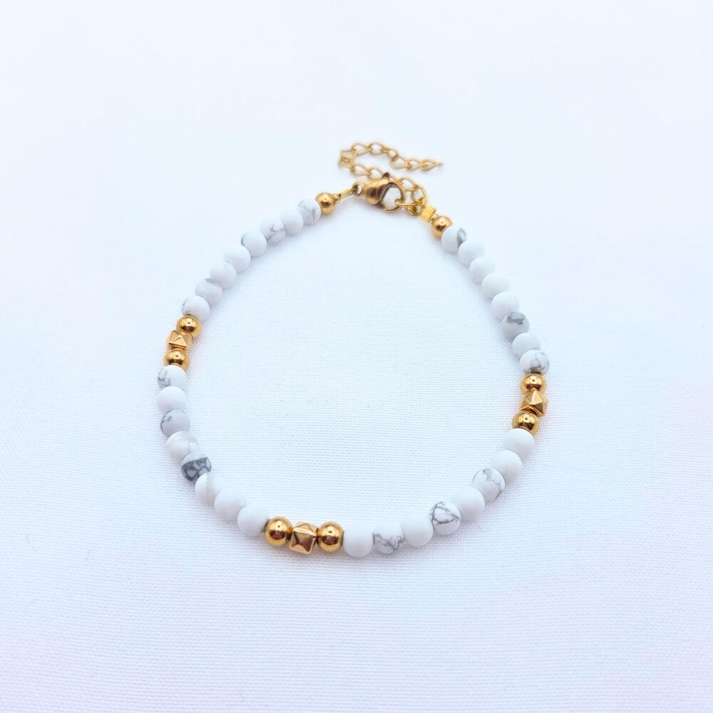 Bracelet fin en perles de Howlite blanche marbrée et détails dorés, fermoir mousqueton ajustable.