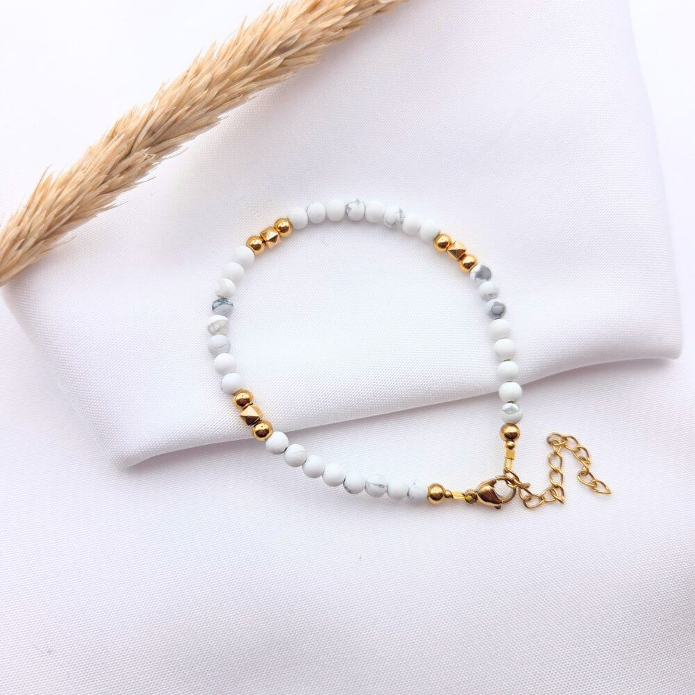 Bracelet fin en perles de howlite blanche et pépites dorées, avec fermoir mousqueton et chaînette d'extension sur fond blanc
