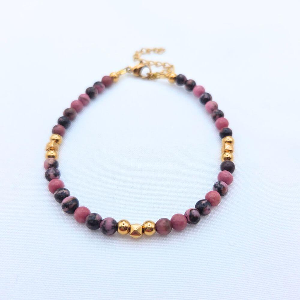 Bracelet en perles de rhodonite rose et noire avec détails dorés et fermoir ajustable.