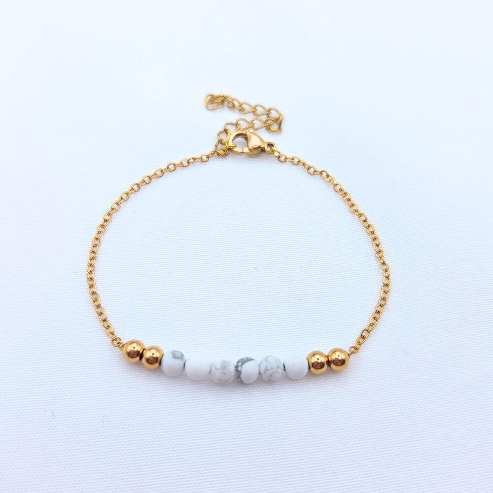 Bracelet fin en chaîne dorée orné de perles de howlite blanche marbrée et de perles d'acier inoxydable dorées.