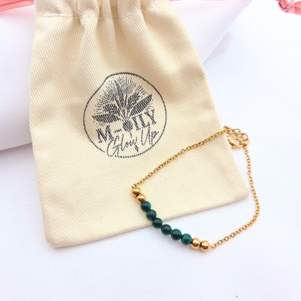 Bracelet doré en maille fine avec perles de malachite verte et billes dorées posé sur un pochon en coton beige "M-ily Glow Up"