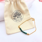 Bracelet doré en maille fine avec perles de malachite verte et billes dorées posé sur un pochon en coton beige "M-ily Glow Up"