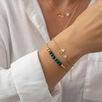 Femme portant une superposition de bracelets dorés, l'un avec des perles de malachite verte et l'autre avec un pendentif cœur et des pierres d'opale.