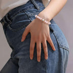Gros plan sur le poignet d'une personne portant un bracelet de perles délicat.

Le bracelet est composé de perles rondes en quartz rose translucide, avec une unique perle bleu ciel au centre, encadrée de deux petites perles dorées. La main repose sur la hanche, vêtue d'un jean bleu classique. L'éclairage est doux, mettant en valeur la texture lisse des pierres et le grain du tissu en denim.