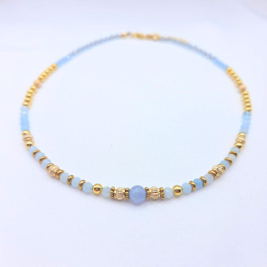 Collier artisanal Ondine de la marque M-ily Glow Up, composé de perles d'Aigue-marine bleu clair et de billes dorées ciselées sur fond blanc.