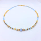 Collier artisanal Ondine de la marque M-ily Glow Up, composé de perles d'Aigue-marine bleu clair et de billes dorées ciselées sur fond blanc.