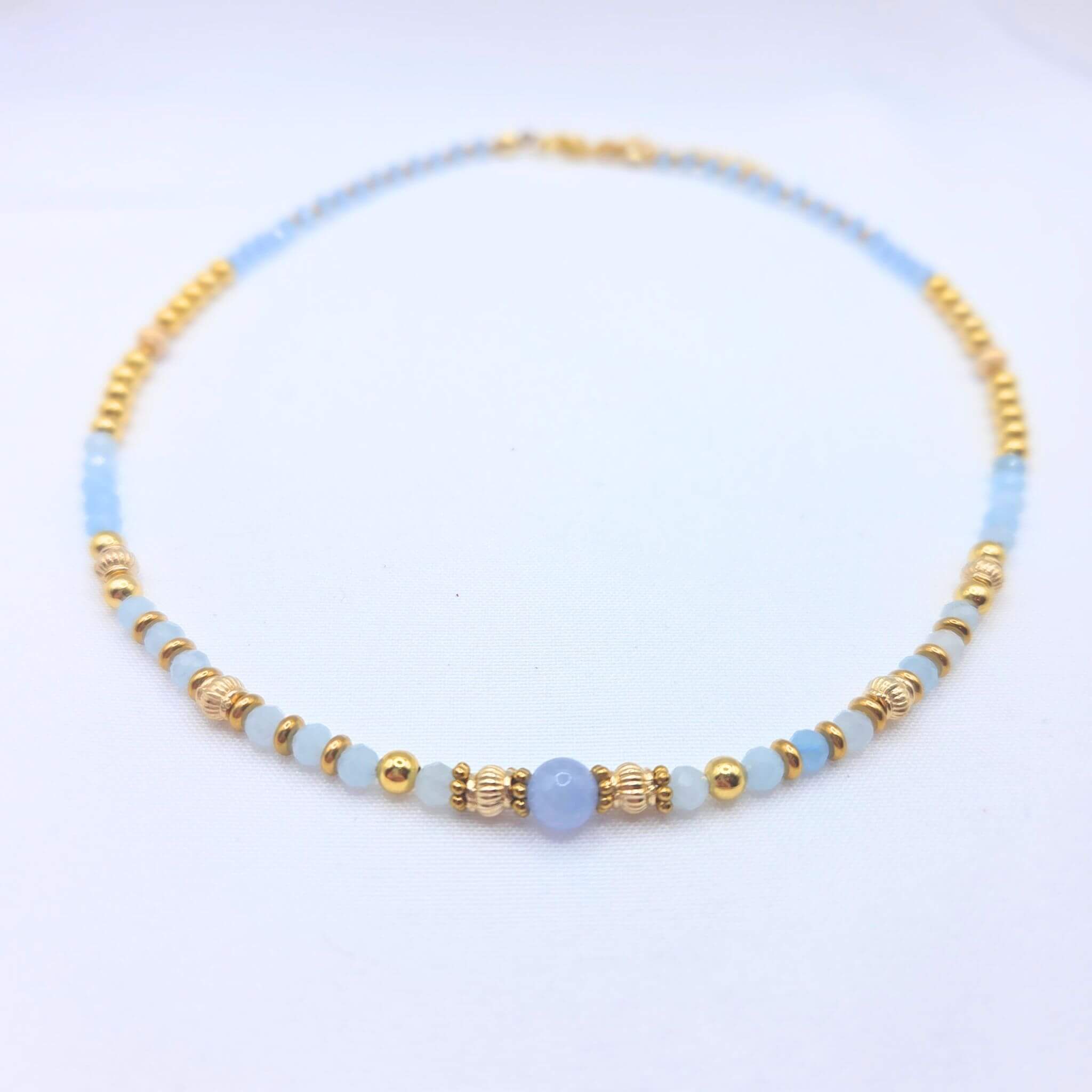 Collier artisanal Ondine de la marque M-ily Glow Up, composé de perles d'Aigue-marine bleu clair et de billes dorées ciselées sur fond blanc.