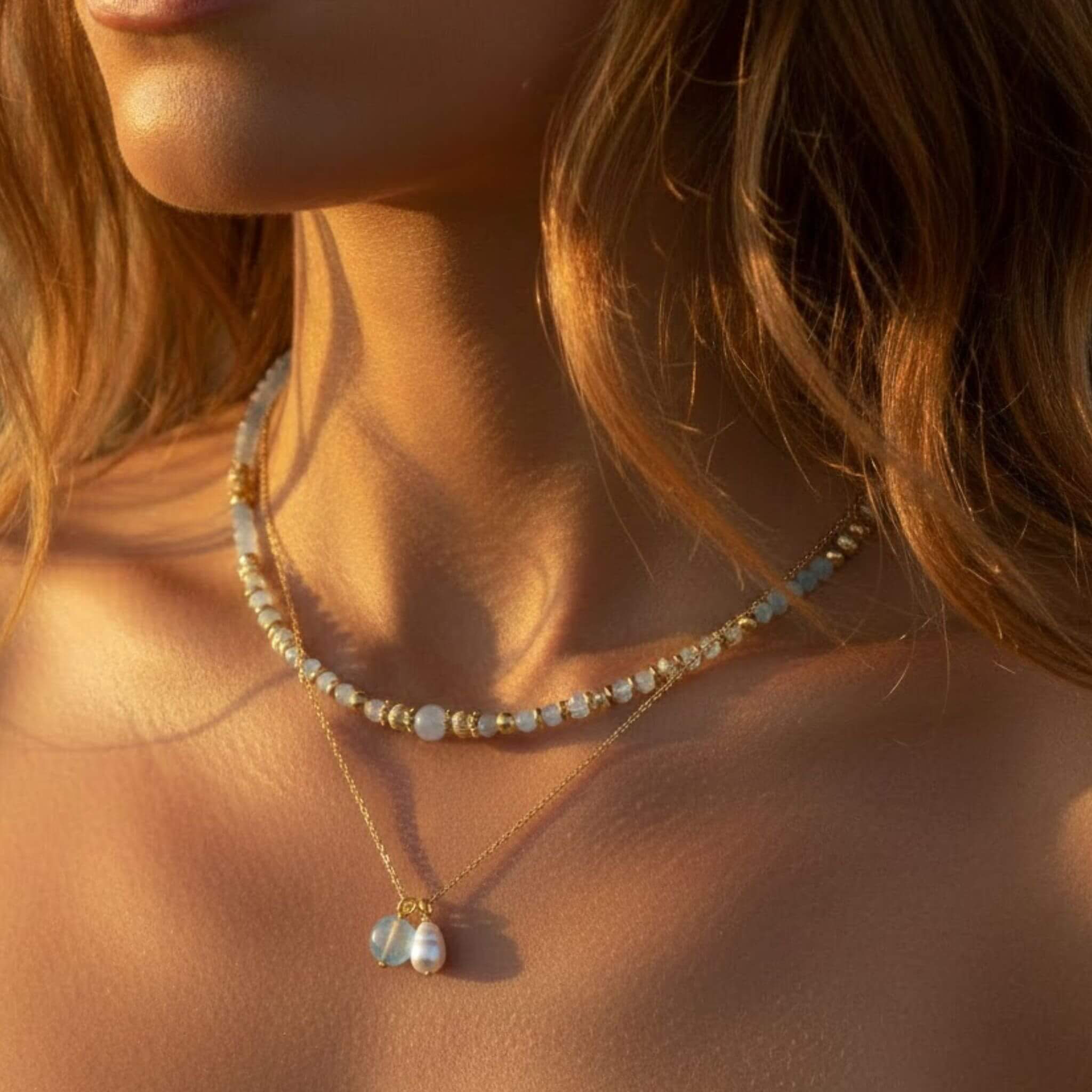 Collier ras-du-cou en perles bleues et dorées avec pendentif perle de culture et pierre bleue. Style bijoux bohèmes chic en lumière naturelle.