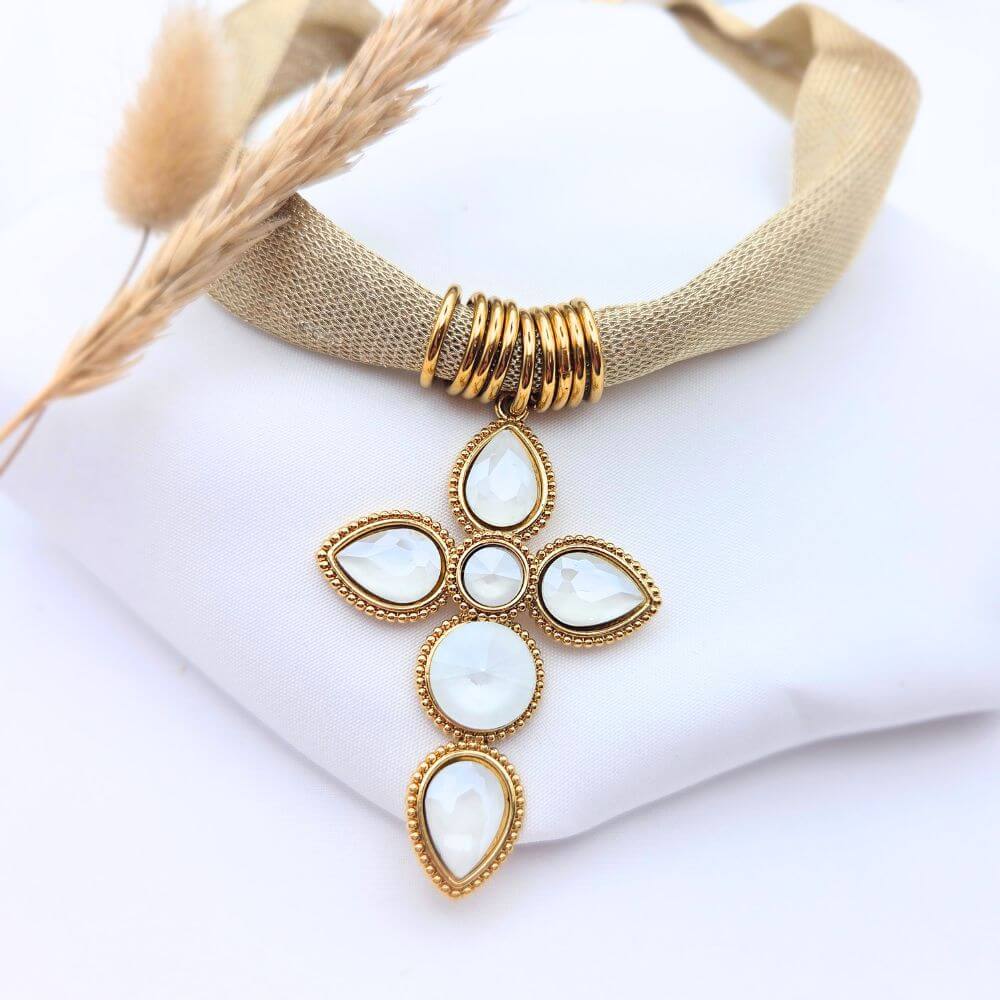 Collier Cléo en acier doré avec chaîne à mailles torsadées et pendentif médaillon rond texturé, présenté sur un tissu blanc avec un épi de blé.