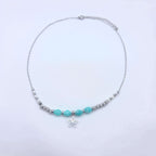 Collier artisanal composé d'une fine chaîne argentée ornée de perles en pierres naturelles de Howlite blanche et d'Amazonite turquoise, avec un pendentif central en forme de fleur de lotus évidée.