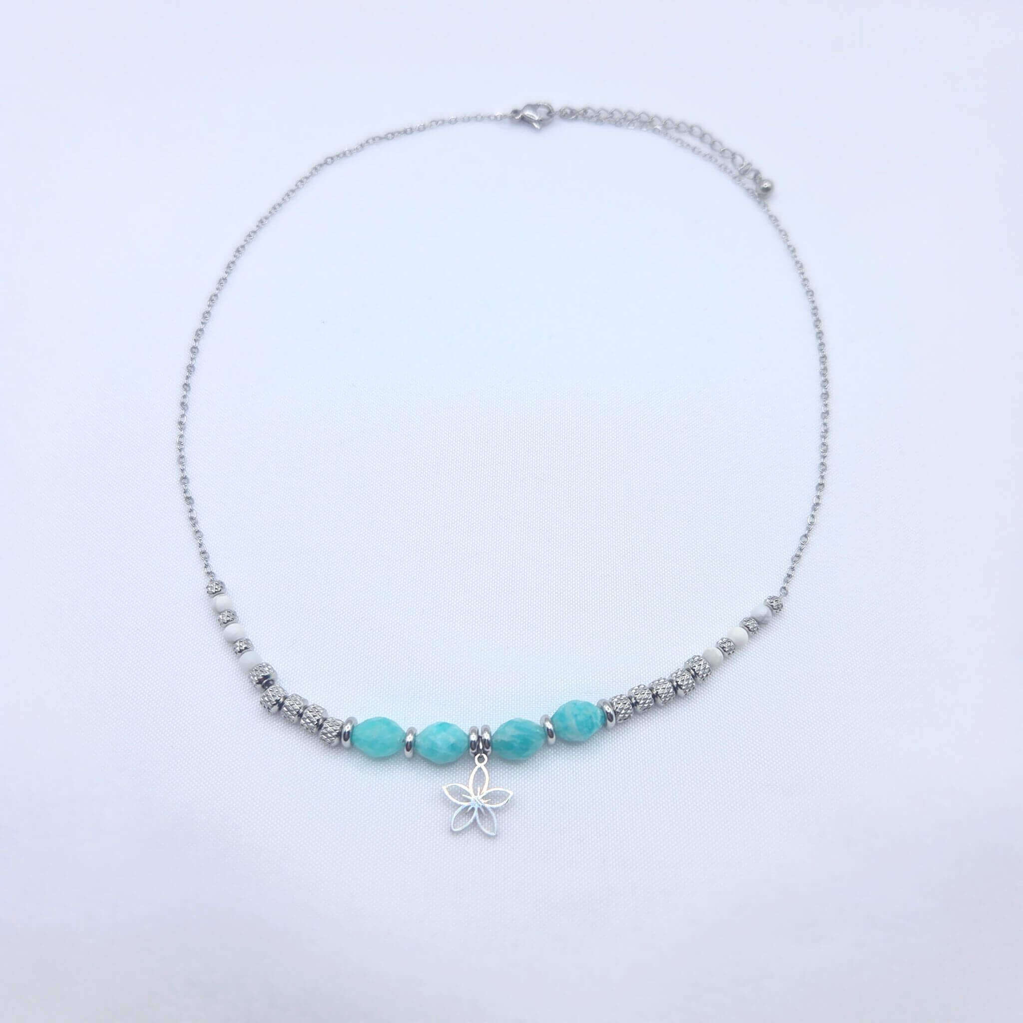 Collier artisanal composé d'une fine chaîne argentée ornée de perles en pierres naturelles de Howlite blanche et d'Amazonite turquoise, avec un pendentif central en forme de fleur de lotus évidée.
