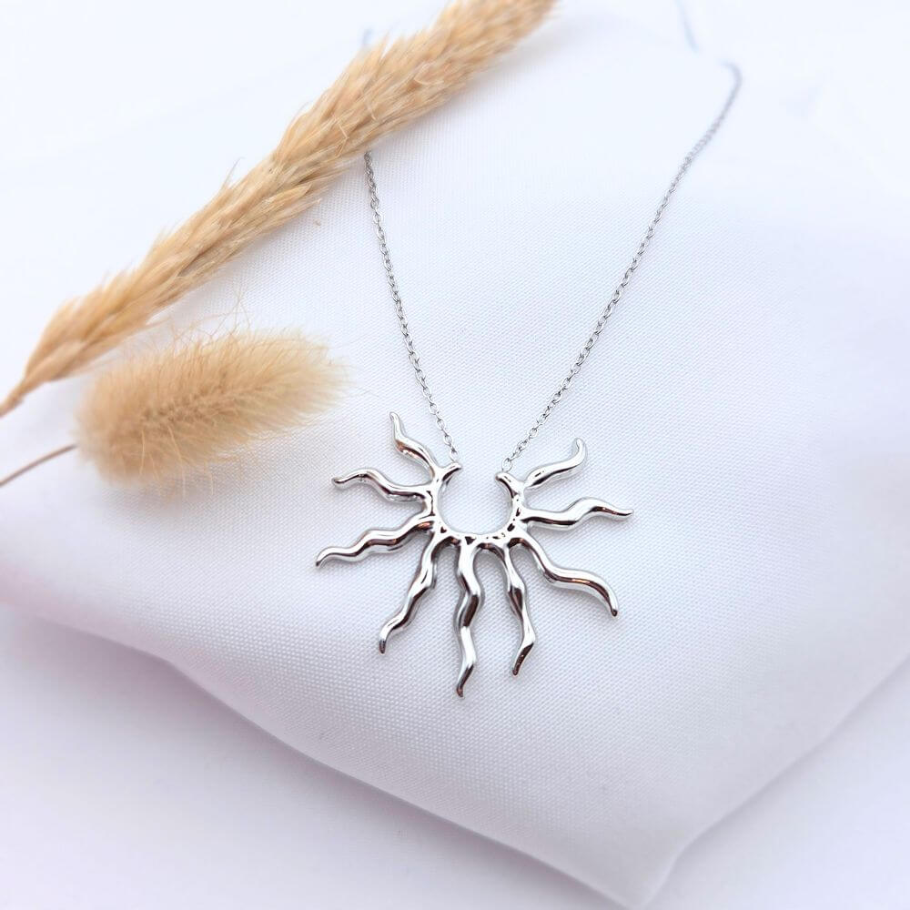 Collier MIMOSA en acier doré avec pendentif médaillon ciselé, posé élégamment sur un tissu blanc avec un épi de blé séché.