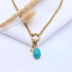 Collier Molly en acier doré avec pendentif goutte en pierre de Jade vert tendre, posé sur un tissu blanc avec un épi de blé séché.