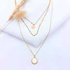 Collier Rivage avec pendentif rectangulaire aux bords irréguliers et martelés, chaîne dorée fine posée sur un tissu blanc avec un épi de blé.