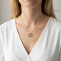 Vue de face d'une personne portant un collier avec une fine chaîne dorée et un pendentif anneau. Le pendentif est composé de perles de lapis-lazuli bleu intense et de petites billes dorées. La personne porte un chemisier blanc col en V, créant un contraste élégant qui fait ressortir le bleu profond des pierres.