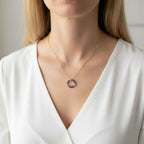 Vue de face d'une personne portant un collier avec une fine chaîne dorée et un pendentif anneau. Le pendentif est composé de perles de lapis-lazuli bleu intense et de petites billes dorées. La personne porte un chemisier blanc col en V, créant un contraste élégant qui fait ressortir le bleu profond des pierres.