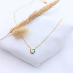 Collier chaîne dorée fine en acier inoxydable avec pendentif cœur en opale australienne blanche aux reflets irisés, présenté sur un tissu blanc avec un épi de blé séché.
