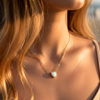 Gros plan d'une femme portant le collier Tess, montrant le pendentif cœur en opale illuminé par la lumière naturelle du soleil sur le décolleté.
