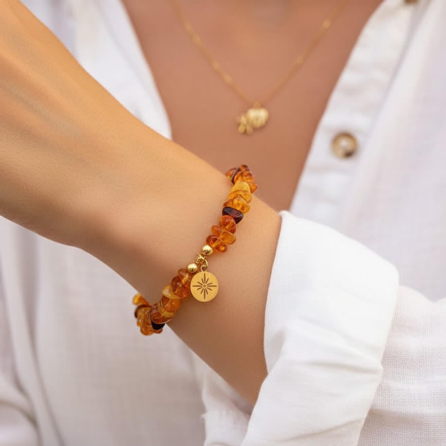 Gros plan sur le poignet d'une personne portant un bracelet en éclats d'ambre aux nuances chaudes de miel et de cognac. Le bijou est orné d'une petite médaille ronde dorée gravée d'une étoile rayonnante.